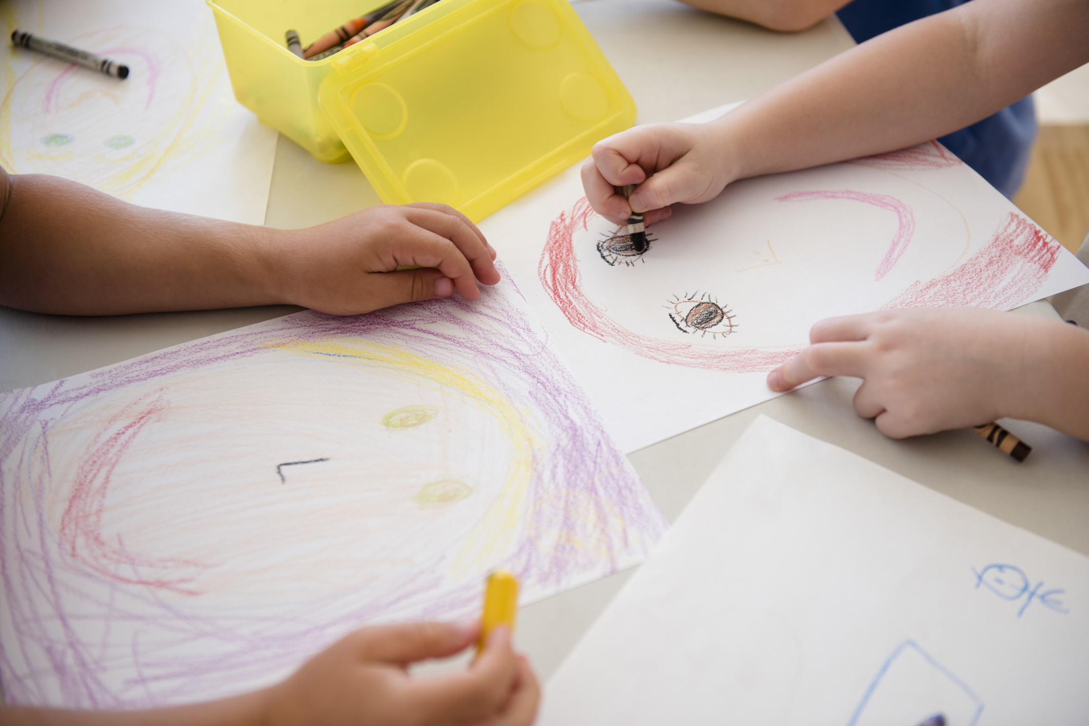 Young children drawing with crayons on paper in a classroom.